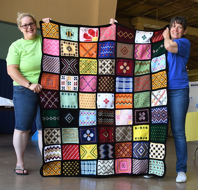 See the bumble bee on the aghan (top row)? This Minnesota sample afghan is the work of Debra Holter of San Pablo. Holding it are McCormack Hall superintendent Gloria Gonzalez (right) and assistant Kara Payne. (Photo by Kathy Keatley Garvey)