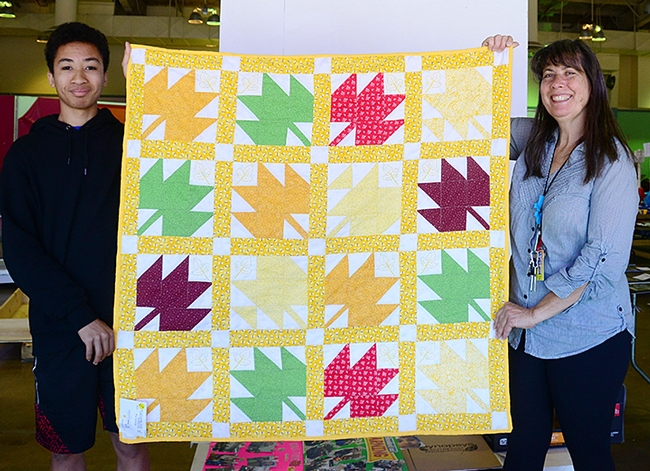 Gloria Gonzalez, superintendent of McCormack Hall at the Solano County Fair, holds a bee-themed quilt with assistant Jarod Fernander of Vallejo, 15, a student at the Pleasant Hill Adventist Academy. The quilt is the work of Tina Frothy of Vallejo. (Photo by Kathy Keatley Garvey)