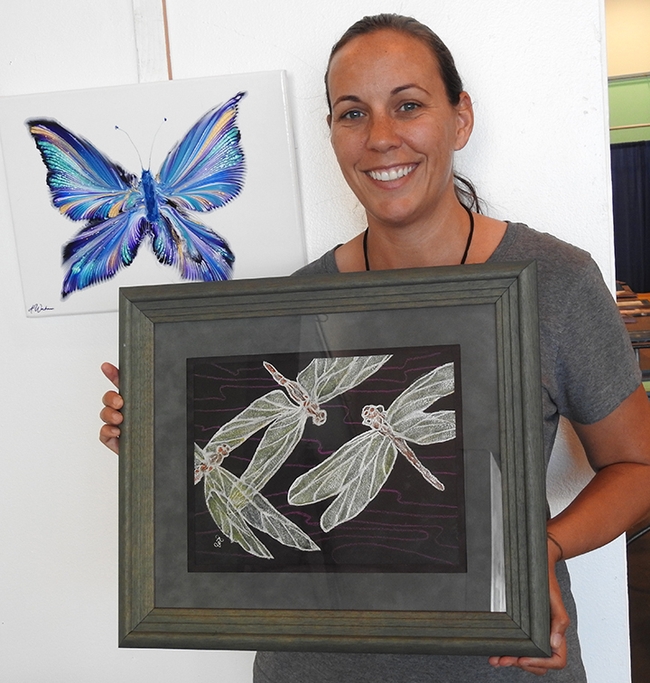 Heather DeGroot of Vallejo, coordinator of the McCormack Hall exhibits, Solano County Fair, shows a watercolor by Richard Laswell of Rio Vista that depicts three dragonflies. In back is an oils-acrylic butterfly by Ashley Workman of Vallejo. (Photo by Kathy Keatley Garvey)