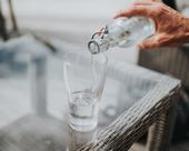 Water pours from a clear bottle into a drinking glass