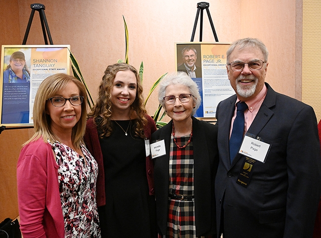 Family members stand in front of a poster honoring Robert E. Page Jr. at the UC Davis College of Agricultural and Environmental Sciences' celebration.  From left are niece Suzi Redmond and her daughter, Emily Redmond; Michelle Page (wife of Rob Page); and the honoree, honey bee geneticist Robert E. Page Jr. (Photo by Kathy Keatley Garvey)