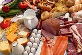 Assorted foods -- vegetables, milk, breads, cheese, eggs, ham, salmon -- on a table.
