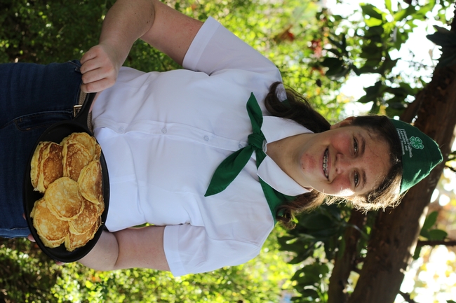 A middle-school girl holds a pan with homemade pancakes on it.
