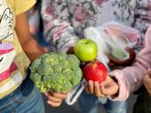 A stalk of broccoli, a green apple and a red apple held in children's hands.