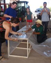 Group hammers plastic to a wooden frame,during construction of a chimney solar dryer in a barn.