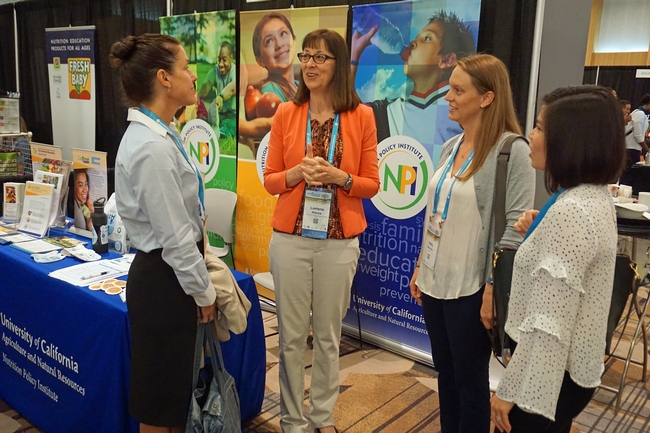 NPI director Lorrene Ritchie, center, talks with colleagues at the Nutrition Policy Institute exhibit at the conference.