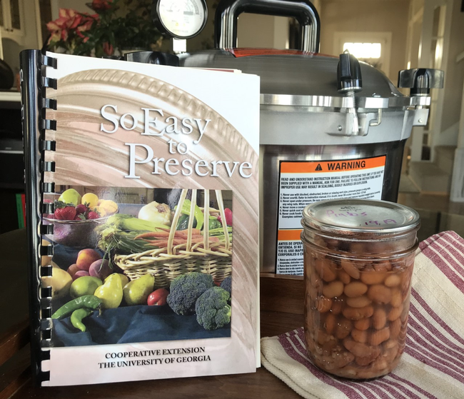So Easy to Preserve recipe book, pressure canner, and finished jar of canned pinto beans