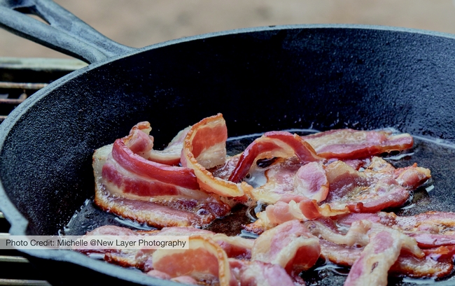 Bacon frying in a black iron skillet.
