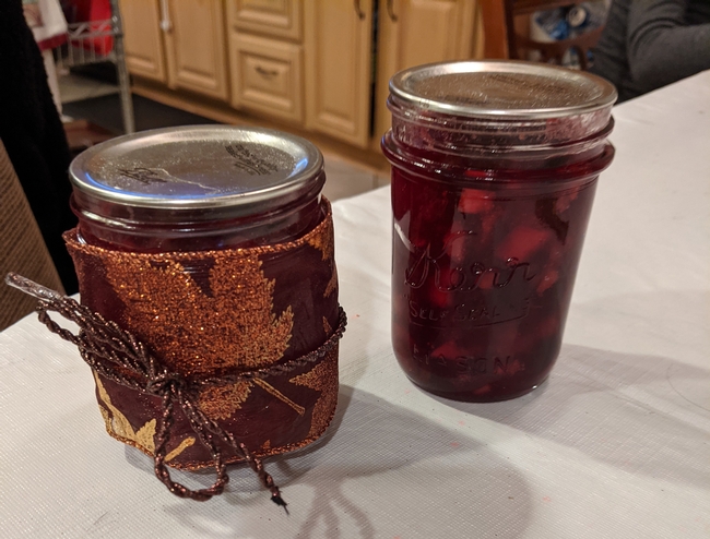Two glass jars, one gift wrapped, the other showing fruit floating in a red liquid.