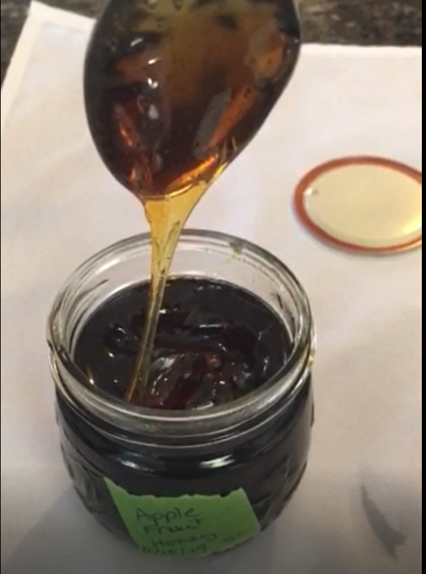 Honey drips from a spoon held above a jar.