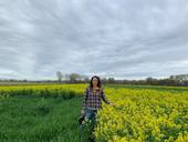 Sarah stands between a green field and yellow flowering mustard.