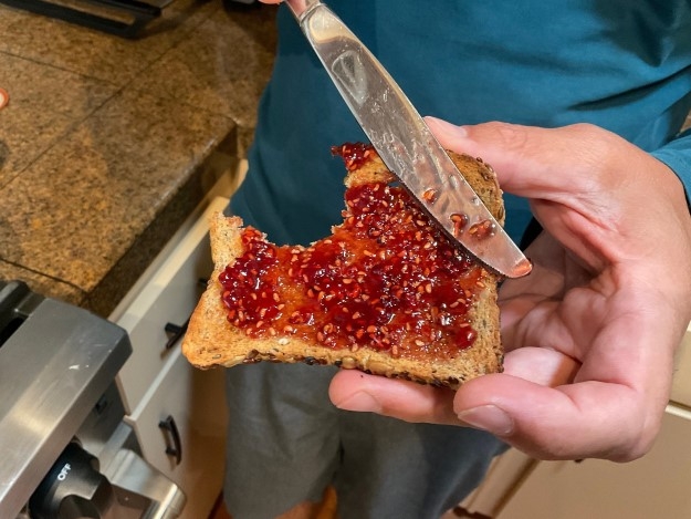 A hand holding a piece of toast with the raspberry jam spread on it.