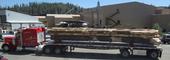 Flat bed log truck arriving at Trinity River Lumber with the new sawmill building in the background,