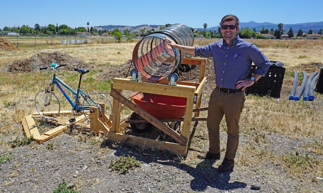 Coordinator of the UCCE composting program in Santa Clara County, Cole Smith, stands with a bicycle-powered compost turning tool at the demonstration site.