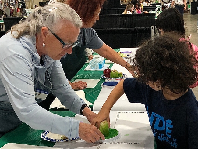 IN foreground Master Gardener helping an elementary schooler stamp a 