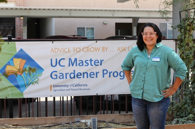 Woman in a teal top standing in front of a UC Master Gardener sign.