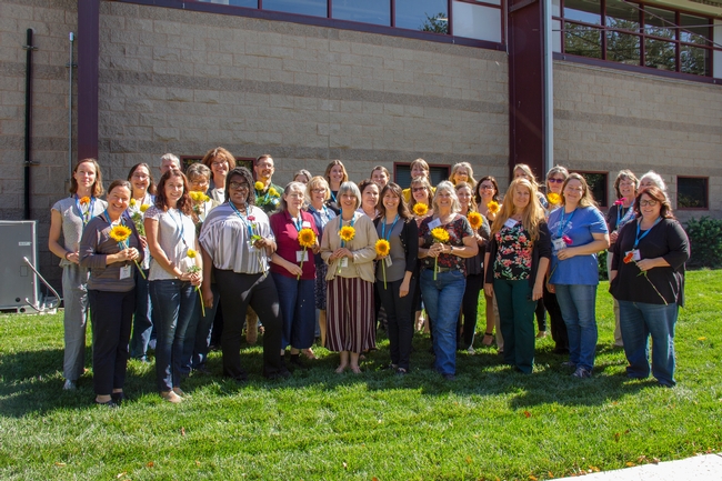 38 team members of the UC Master Gardener Program taking a group photo, holding sunflowers, in front of the UC ANR building.