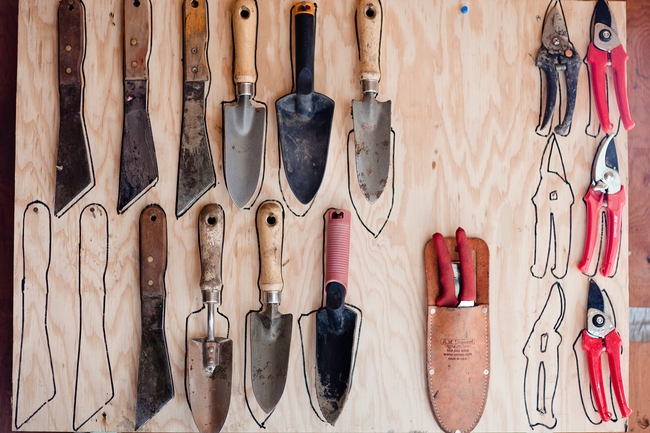 trowels, pruners, and garden blades hanging on a board