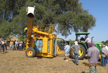 A group of farmers looking at a stationary mechanical grape harvester.