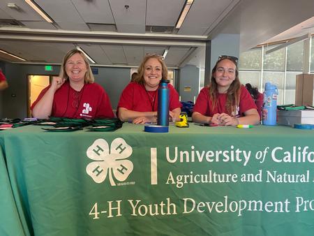 Three 4-H adults are sitting at a 4-H branded table. Helping as chaperones