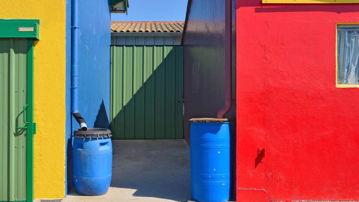 Colorful rain barrels attached to downspouts harvest roof water for use in the garden. Credit: Wikimedia Commons