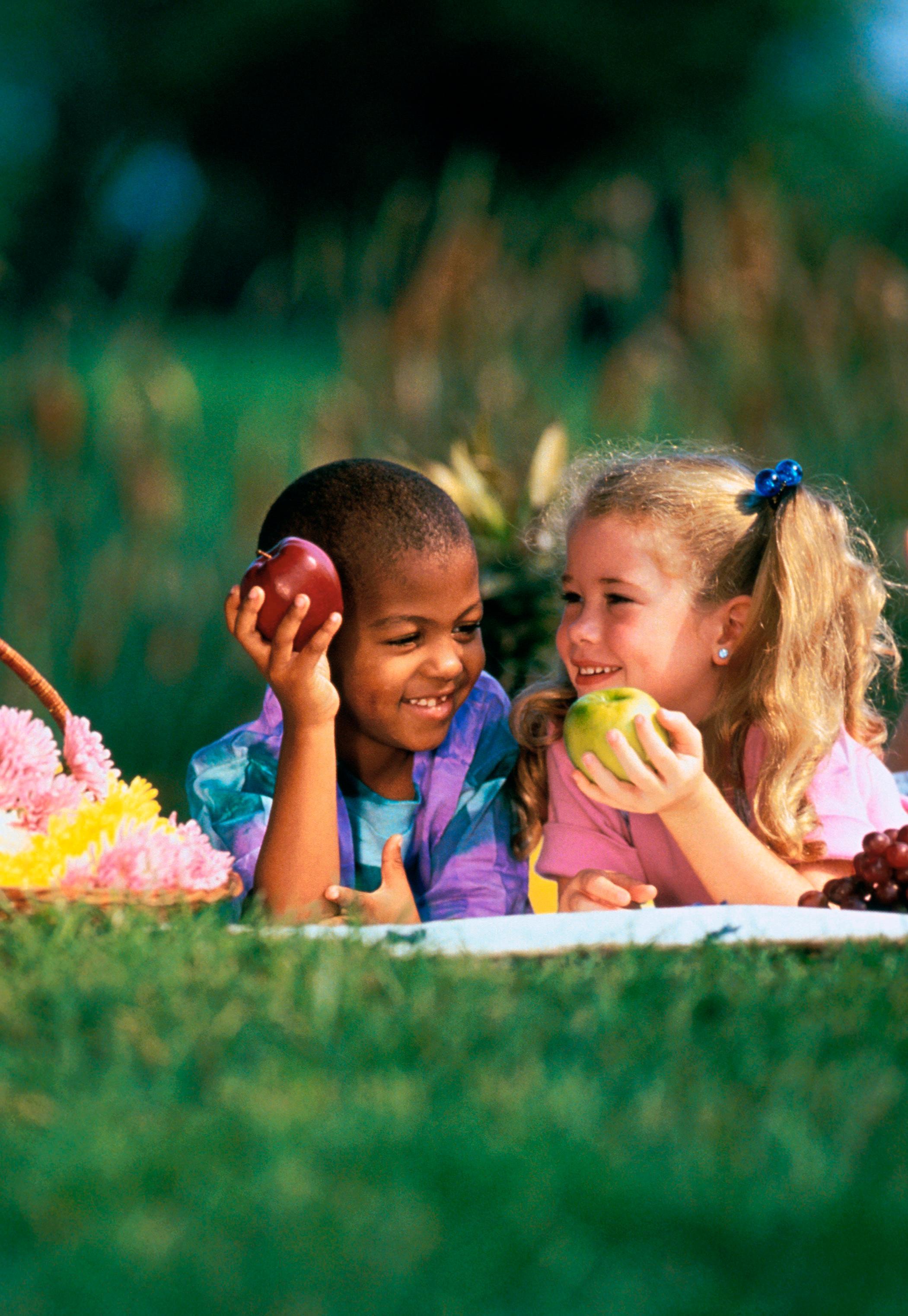 Niño y niña joven disfrutando unas manzanas en el pasto.