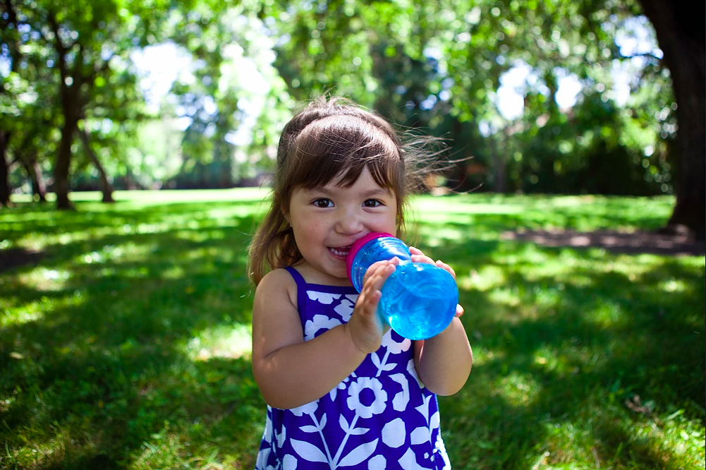 Niña joven bebiendo agua de una botella.