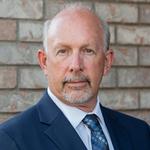 A photo of Dave Green with a gray background, he is wearing a gray suit