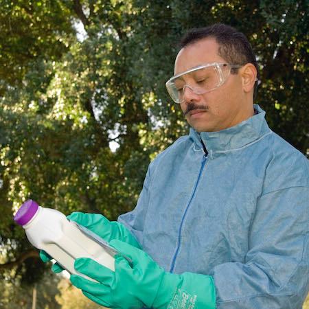 Man in long-sleeved shirt, eye protection, and gloves reading pesticide label instructions. Credit: Michael L. Poe, UC Agriculture & Natural Resourced