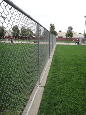 A fence with grass on either side at a dog park in Irvine. Weeds and encroaching grass are controlled with a mechanical edger instead of herbicide.