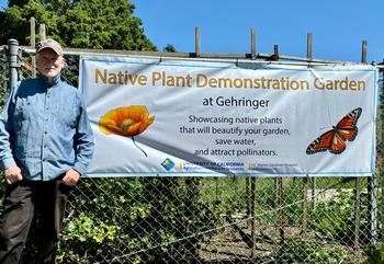 UC Master Gardener Phil Quinlan stands next to the Gehringer Demonstration Garden sign highlighting native plants. Photo by Allison Thomas.