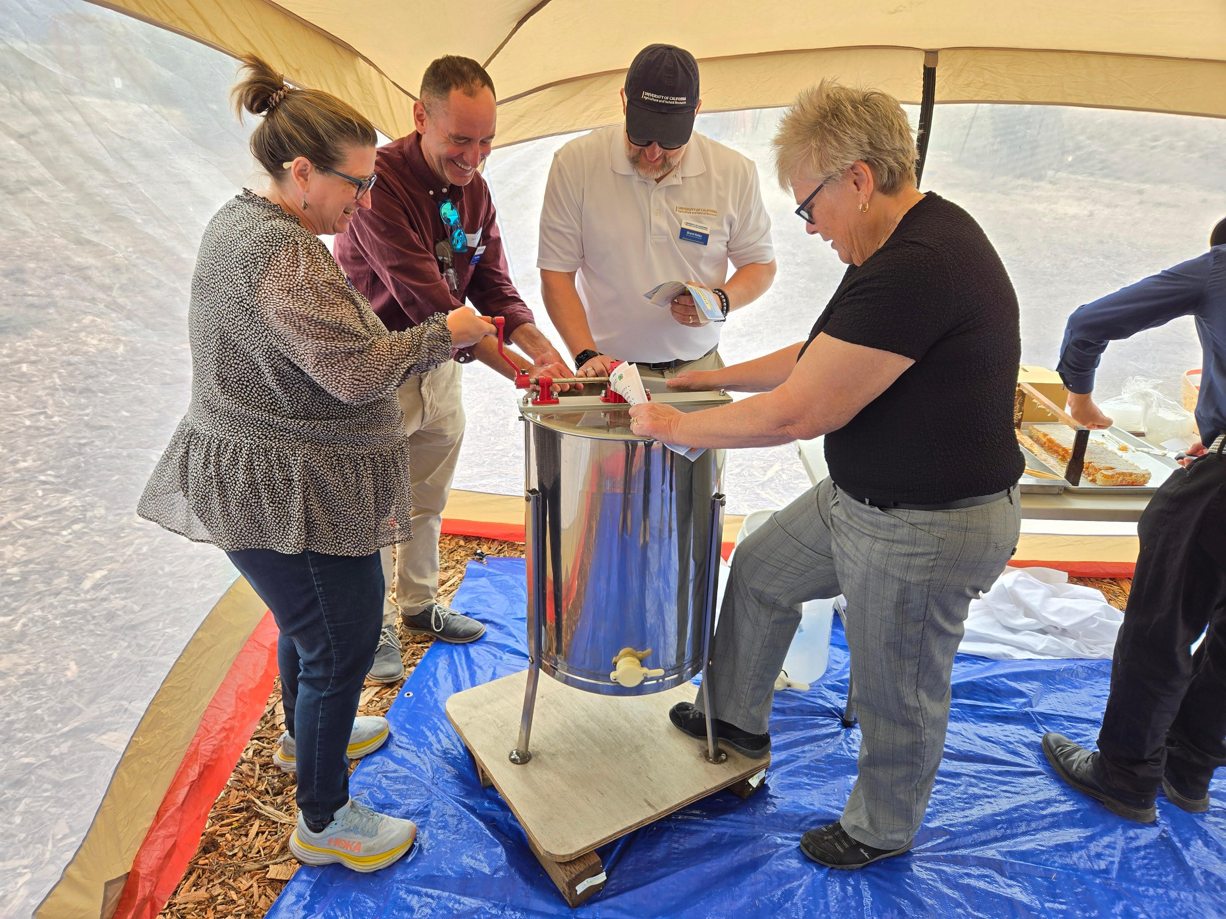 Elizabeth, Daniel, Brent, and Lynn try their hand using a honey extractor