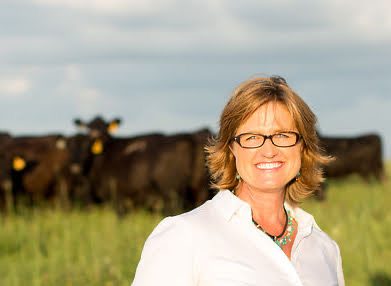 Debbie Lyons-Blythe in a pasture with cows behind her.