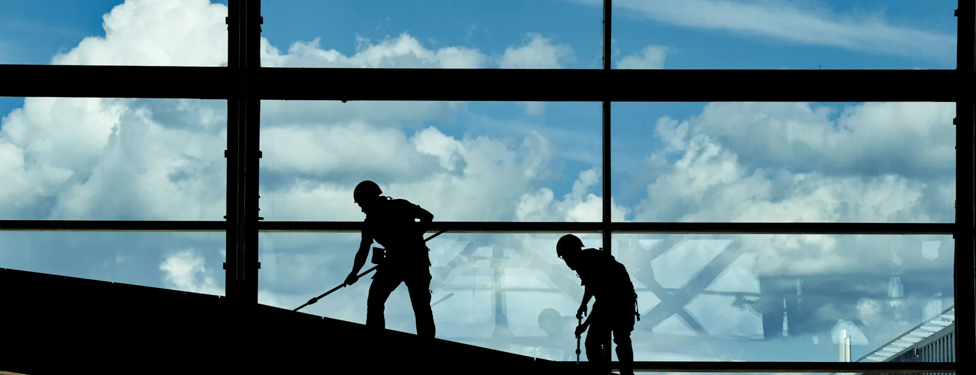 Window cleaners in shadows with sky background past the glass