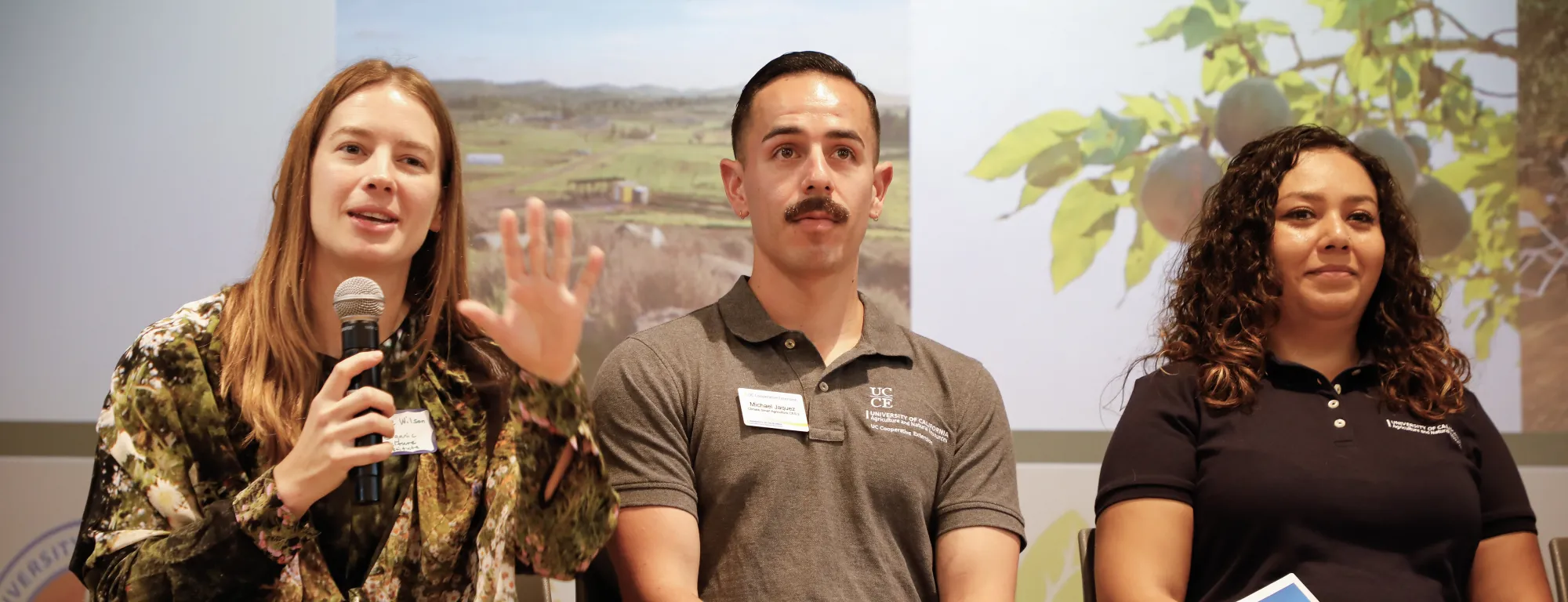 Three people sit on stage in front of a screen, speaking to an audience