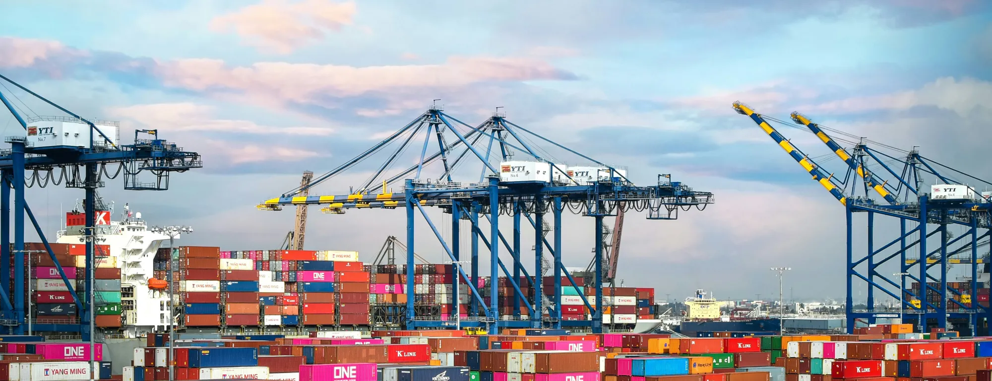 The Port of Los Angeles filled with brightly colored shipping containers and a container ship docked next to cranes.