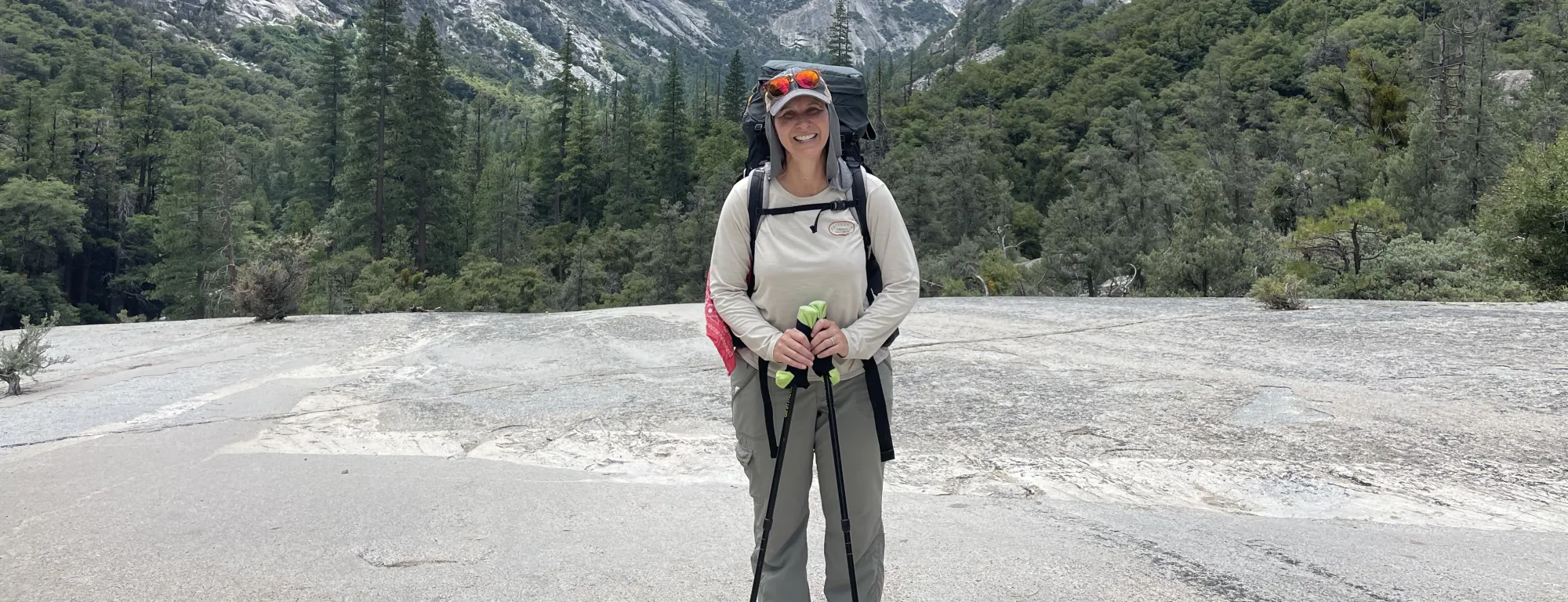 Kristin Polidoro stands with hiking poles, with Kings Canyon behind her and the South Fork of the Kings River below, unseen