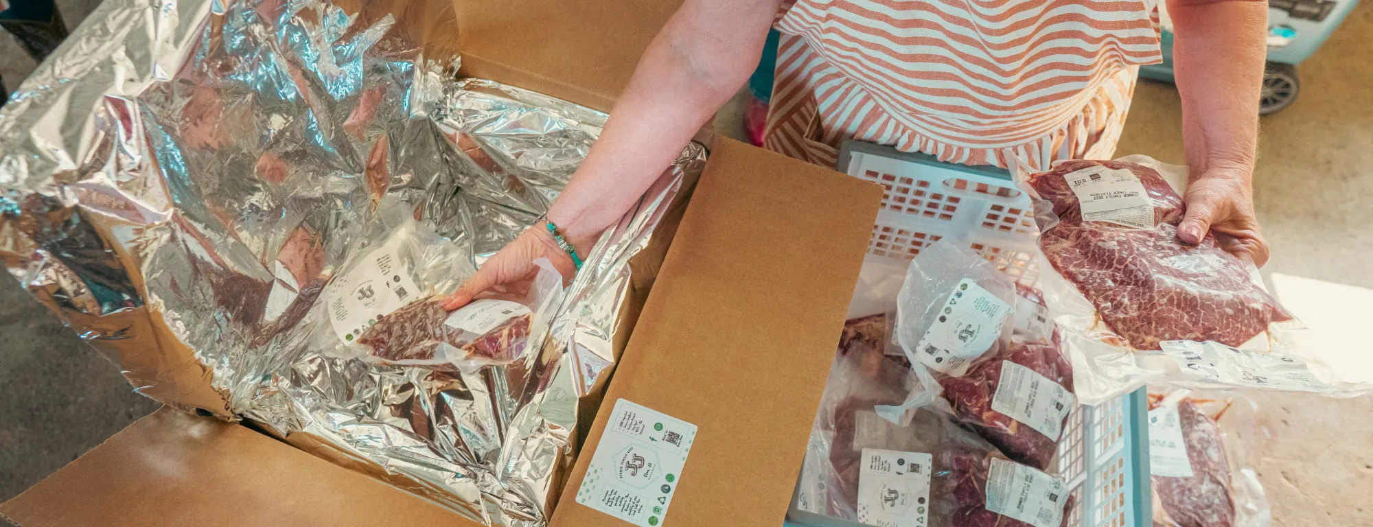 A person wearing an apron places vacuum-packed beef into a lined cardboard shipping box.