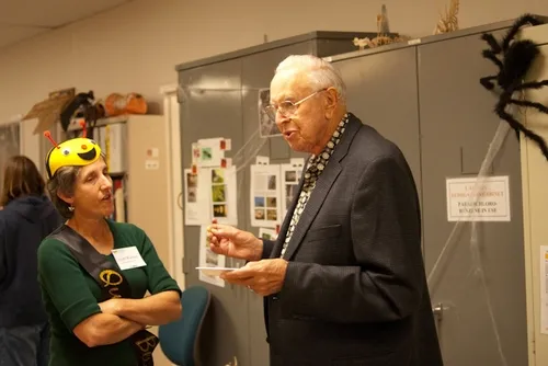 QUEEN BEE Lynn Kimsey, director of the Bohart Museum of Entomology and professor and former chair of the UC Davis Department of Entomology, chats with emeritus professor and entomologist Oscar Bacon of Davis, also a former chair of the department. A black widow spider hovers in the background. (Photo by Louie Yang)