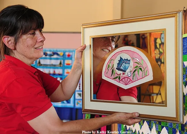 Gloria Gonzalez hangs a needlepoint fan, the work of Laura Ryan of Benicia. Note the blue butterfly. (Photo by Kathy Keatley Garvey)