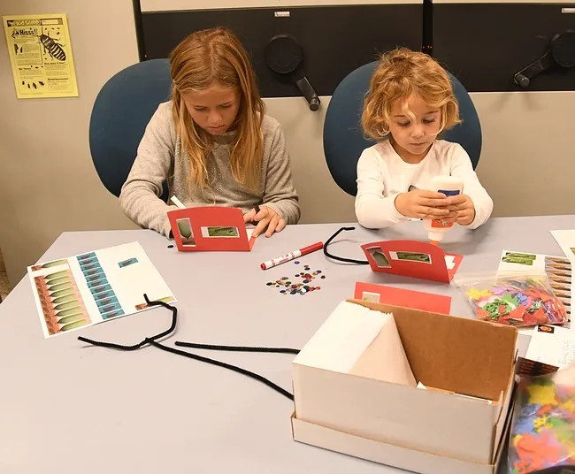 Sisters Zia Tinel, 8, and Olivia Tinel, 4, of Davis engage in the family craft activity: making pop-up cards starring monarchs and parasitoids. (Photo by Kathy Keatley Garvey)