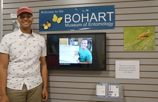 Noah Crockette stands by a wall-mounted computer screen with an image of him at age 14. (Photo by Kathy Keatley Garvey)