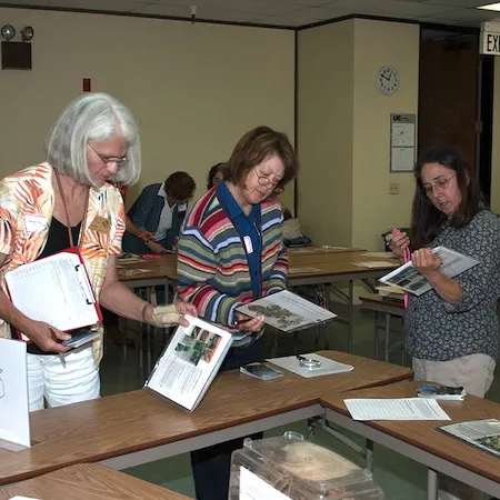 Three women look at preserved plant samples showing symptoms of pests in a classroom. Credit: Cheryl Reynolds, UC IPM