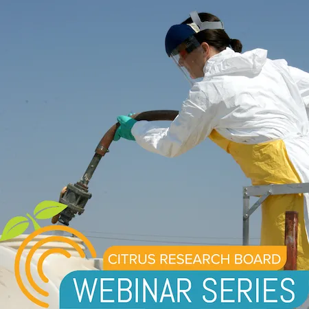 A person filling a large tank with water while wearing chemical-resistant gloves, coveralls, and other personal protective equipment.