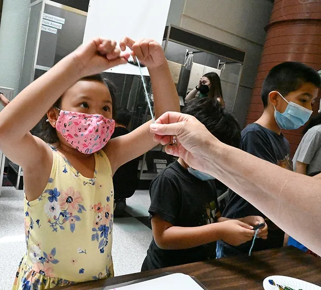 A participant combs yarn as part of the hands-on activity in the sticky vs. non-sticky spider silk station. (Photo by Kathy Keatley Garvey)