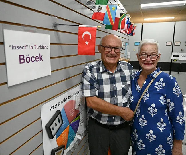At the Bohart Museum of Entomology, Dr. Ismail Seker and his wife, Esin, stand in front of the Turkish flag and a card indicating how to say "insect" in the Turkish language. The Bohart Museum spotlights a global collection of flags, as well as how to say "insect" in many languages. (Photo by Kathy Keatley Garvey)
