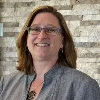 Woman with glasses and gray jacket, with a gray background