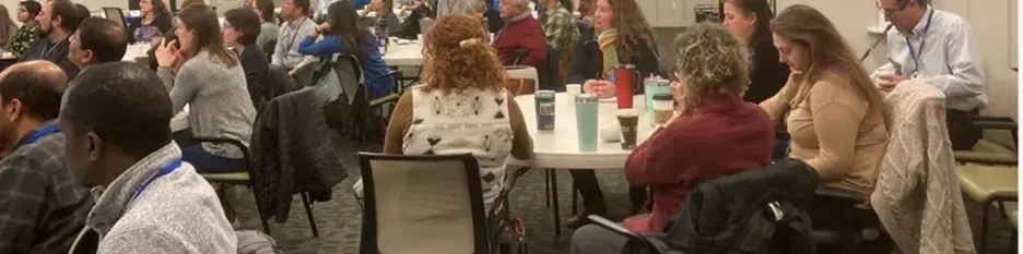Employees seated at tables during a meeting, engaged in discussion and listening.