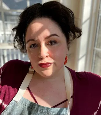 Teresa Finney is wearing an apron and a dark red sweater. 