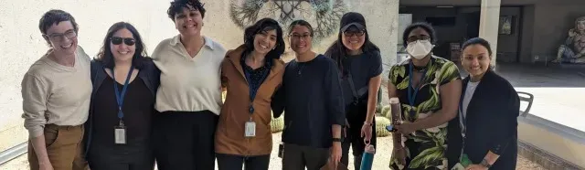 A group of eight smiling people stand side by side, posing for a photo.